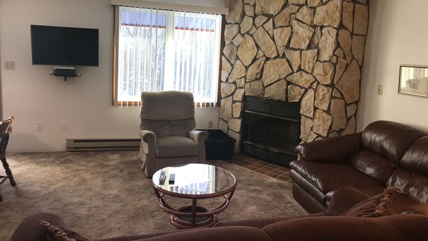 A living room with a stone fireplace, a television mounted on the wall, a comfortable leather sofa, and a cushioned armchair. - 9 - Clean, Comfortable and Quiet Condo at the base of Jackson Creek Summit (Wakefield)