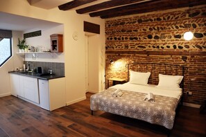 Una habitación compacta con kitchenette, una cama con colcha estampada y una pared de piedra.