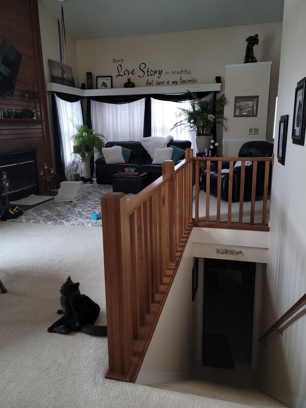 Un salon avec un canapé noir, un escalier en bois et un chat sur le sol.