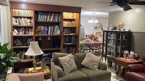 A living room with a sofa, a coffee table, a bookshelf, a dining table, and a chandelier.