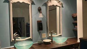 A bathroom with two large mirrors, a glass bowl sink, and a towel rack.