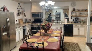 A modern kitchen with stainless steel appliances, a dining table set for four, and a chandelier.