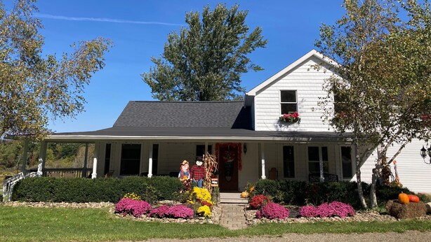 A white house with a gabled roof, a front porch, and a garden with various flowers and plants.