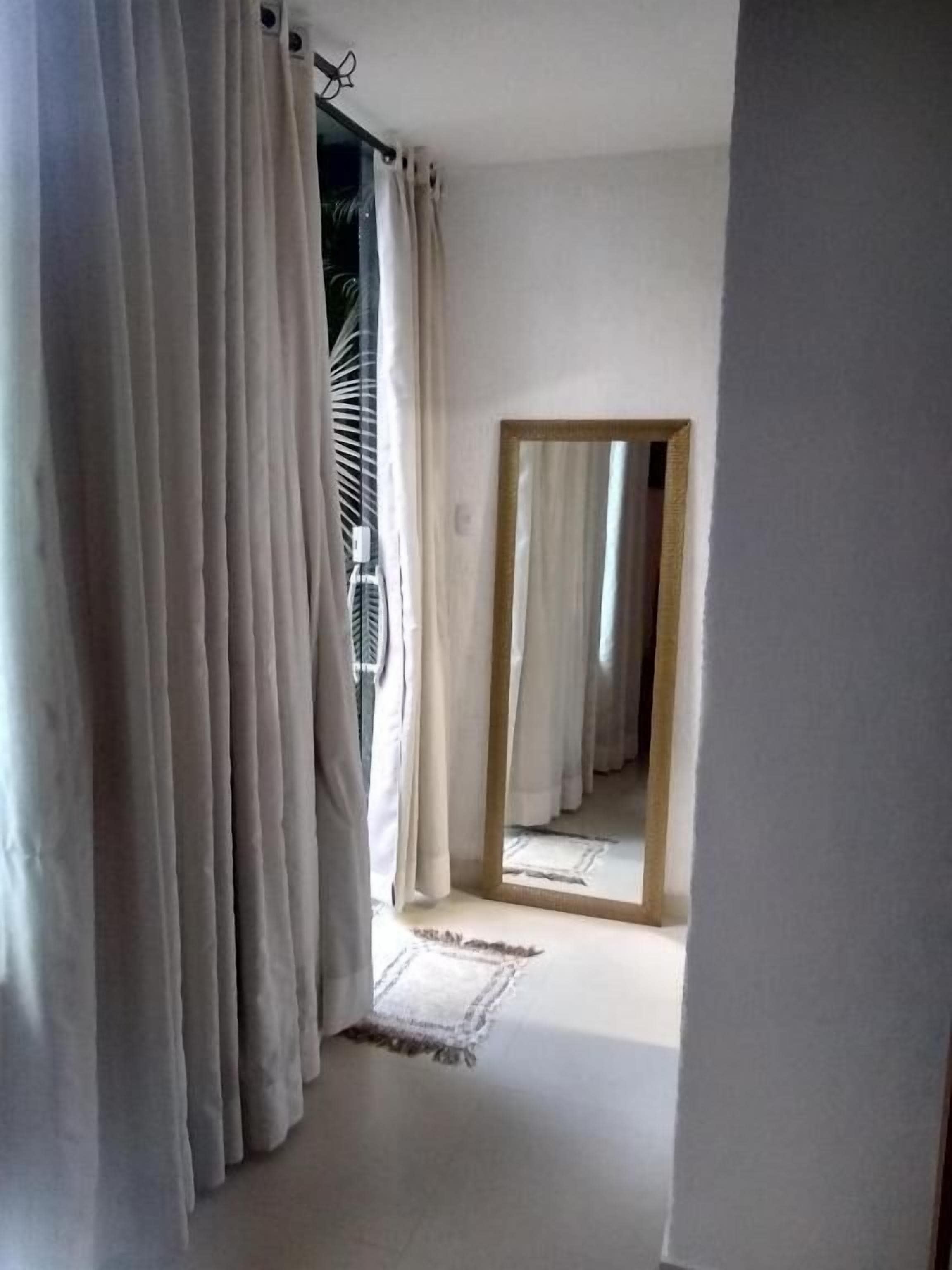 Un pasillo con un espejo que refleja una habitación, un ventilador de techo y una alfombra en el suelo.