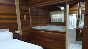 A wooden-paneled room with a bed, a large mirror, and a bathroom visible through a glass door. - Pousada do Lago Petrópolis (Petrópolis)