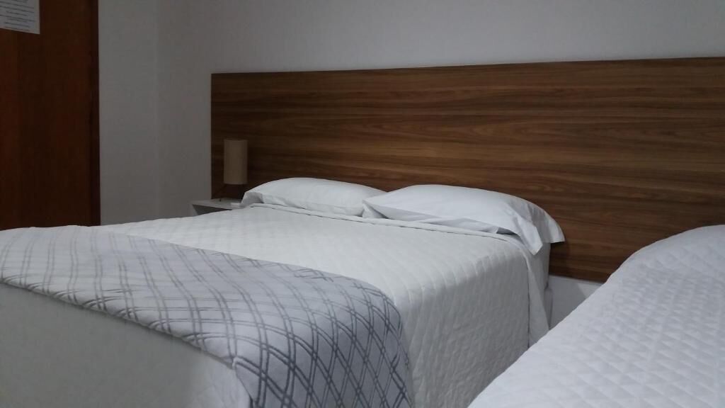 Une chambre d’hôtel avec deux lits, une tête de lit en bois et une table de chevet avec une lampe.