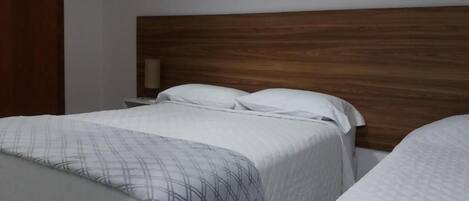 Une chambre d’hôtel avec deux lits, une tête de lit en bois et une table de chevet avec une lampe.