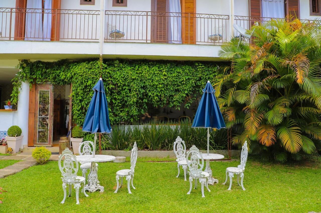 A courtyard with white ornate chairs and tables, blue umbrellas, and lush greenery.