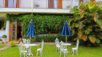 A courtyard with white ornate chairs and tables, blue umbrellas, and lush greenery.