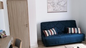 Ein Wohnzimmer mit einem blauen Sofa, einer Holztür, einer Karte an der Wand und einem Tisch mit einer Fernbedienung.