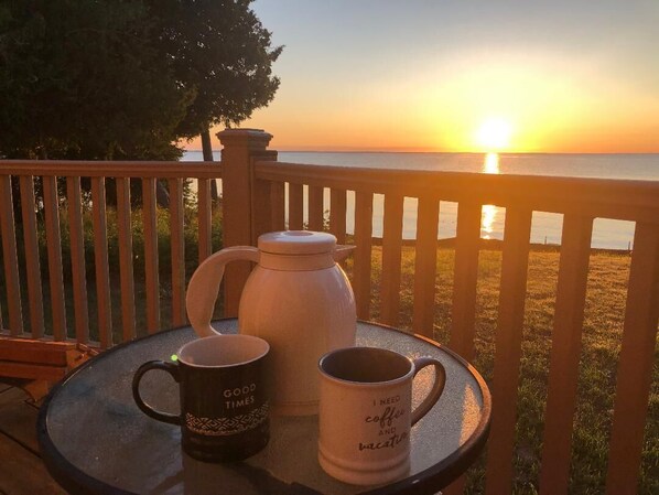 Una mesa con dos tazas de café y una cafetera blanca en un balcón con vista a la puesta de sol.