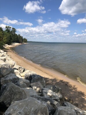 A beach with large rocks in the foreground, a sandy shore, and a calm sea under a partly cloudy sky.