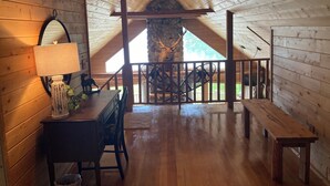 A wooden interior with a dining table, chairs, a lamp, a stone wall with antlers, and a staircase leading to a balcony. - Pure Michigan on Lake Michigan-Manistique, miles of sandy beach fun (Manistique)