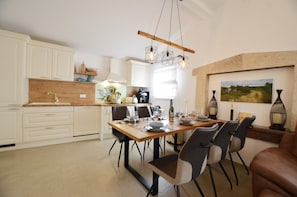 Ett modernt kök med vita skåp, ett träbord med plats för fyra personer och en hängande lampa.