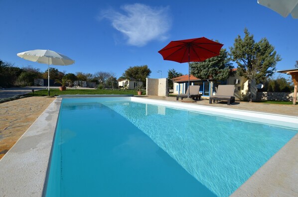 A swimming pool with two umbrellas, a patio area, and a view of the surrounding landscape.