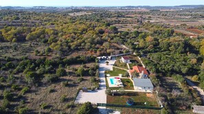 An aerial view of a property with a swimming pool, a tennis court, and a fenced garden area.