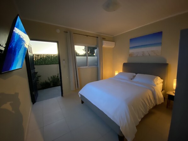 A bedroom with a bed, a TV mounted on the wall, and a window with curtains.