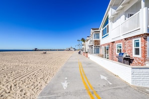 A beachfront hotel with a concrete walkway leading to the beach, featuring a row of rooms with brick facades and balconies. - Beautiful Downstairs Unit Oceanfront Property! (Newport Beach)