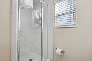 A shower with a glass door, white tiled walls, and a window with blinds. - Beautiful Downstairs Unit Oceanfront Property! (Newport Beach)