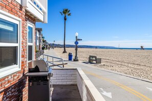 A beachfront property with a barbecue area, a street sign, and a beach in the background. - Beautiful Downstairs Unit Oceanfront Property! (Newport Beach)