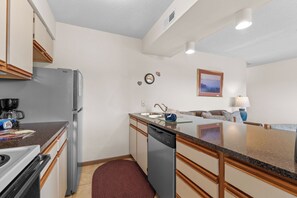 A compact kitchen with a refrigerator, coffee maker, dishwasher, and a dining area with a couch and table.
