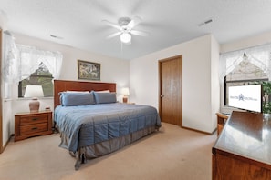Une chambre à coucher avec un lit, des tables de chevet, une lampe, un ventilateur de plafond et une porte.