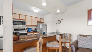 A compact kitchen with a microwave, stove, refrigerator, and a coffee maker. There are two wooden chairs and a brown leather sofa. - Fantastic Lake Views, Large Deck, Boat Slip Included & Free SDC Tickets (Branson)