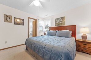 A bedroom with a large bed, a wooden nightstand, a lamp, and a ceiling fan.