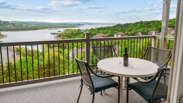 A balcony with a table and chairs overlooking a river and greenery. - Fantastic Lake Views, Large Deck, Boat Slip Included & Free SDC Tickets (Branson)