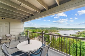 Un balcon avec une table et des chaises, donnant sur une rivière et un paysage verdoyant.