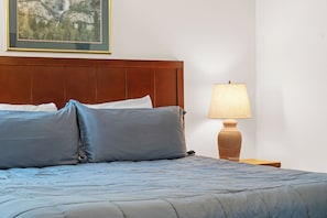 Un lit bien fait, avec une tête de lit, une lampe de chevet et un tableau encadré accroché au mur.
