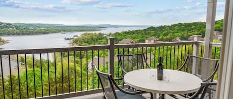 A balcony with a table and chairs overlooking a river and greenery.