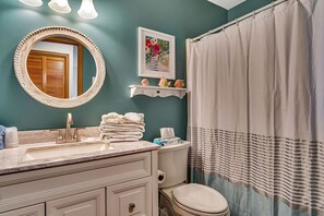 Une salle de bain avec un miroir rond, un lavabo doté d’un plan de toilette en marbre, des toilettes et un rideau de douche.