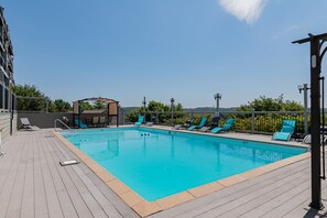 Ein rechteckiger Pool mit Holzterrasse, umgeben von blauen Liegestühlen und einer überdachten Sitzgruppe.