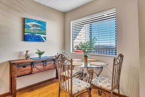 A dining area with a wooden console table, four patterned chairs, a glass table, and a painting above the table.