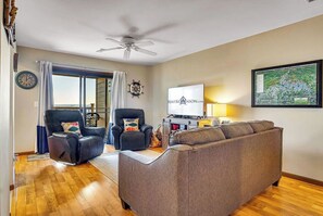 A living room with a grey sofa, two black leather chairs, a ceiling fan, a TV, and a map on the wall.