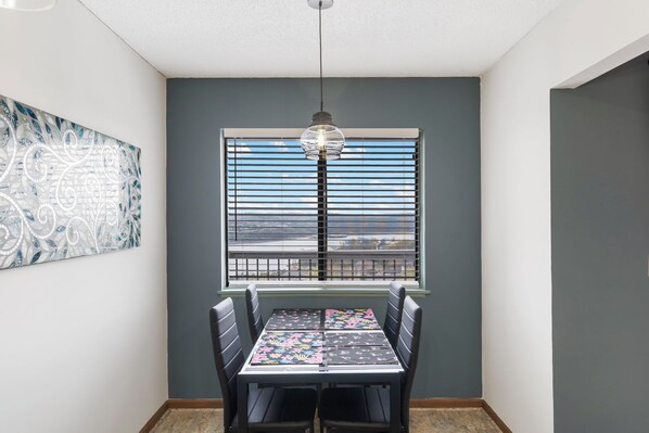 A dining area with a table and chairs, a window with blinds, and a pendant light. - Stunning Table Rock Lake View Condo, Newly Renovated with Free SDC Tickets (Branson)