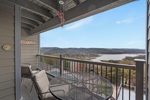 Un balcón con vista a un río y colinas, una silla, una mesa y un letrero que dice 'HAPPY PLACE'.