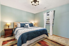 Ein Schlafzimmer mit einem Bett, Nachttischen, einem Deckenventilator und einem Fenster mit Vorhängen.