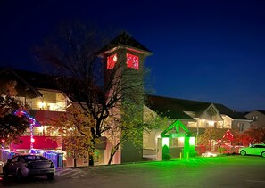 Una zona residencial de noche con casas, un letrero iluminado en verde y un coche estacionado al frente.