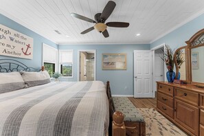 Une chambre à coucher avec un lit, un ventilateur de plafond, une commode, un miroir et un tableau accroché au mur.