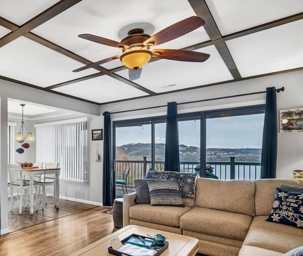 A spacious living room with a large window, a ceiling fan, and a dining area with a table and chairs.