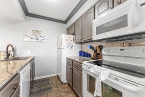 Una cocina con encimeras de granito, refrigerador, estufa y alacenas.