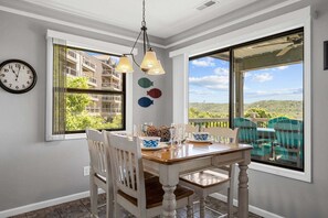 A dining area with a table, chairs, a clock, and large windows with a view.