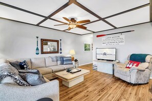 Un salon moderne avec un ventilateur de plafond, un téléviseur, un canapé, un fauteuil et une table basse.