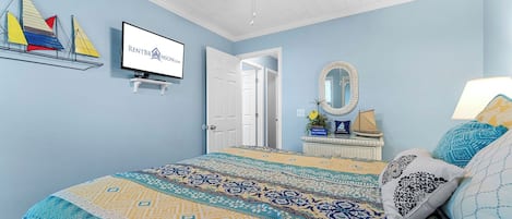 A bedroom with a bed, a television, a door, a mirror, and a shelf with decorative items.