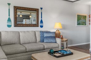 Un salon comprenant un canapé, une lampe, une table basse et des éléments décoratifs sur les murs, notamment un miroir et deux objets en forme de pagaie.