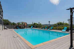 Une piscine rectangulaire avec une terrasse en bois, entourée de chaises longues et d’un espace salon abrité.