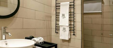 A modern bathroom with a large white sink, a towel rack with multiple towels, and a shower area.