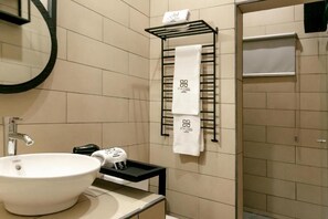 A modern bathroom with a large white sink, a towel rack with multiple towels, and a shower area. - D la Torre Hotel (Managua)